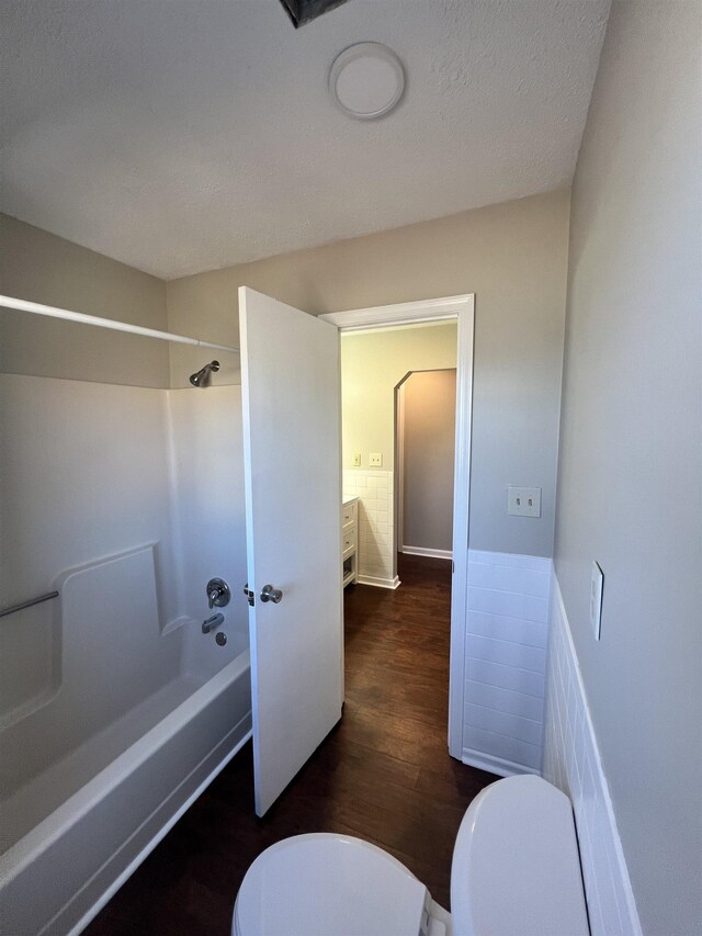 bathroom with bathtub / shower combination, hardwood / wood-style floors, a textured ceiling, and toilet