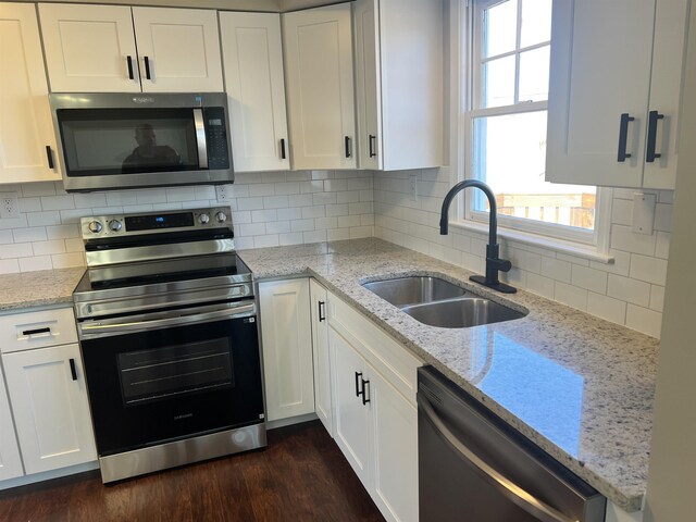 kitchen with sink, white cabinetry, backsplash, stainless steel appliances, and light stone counters