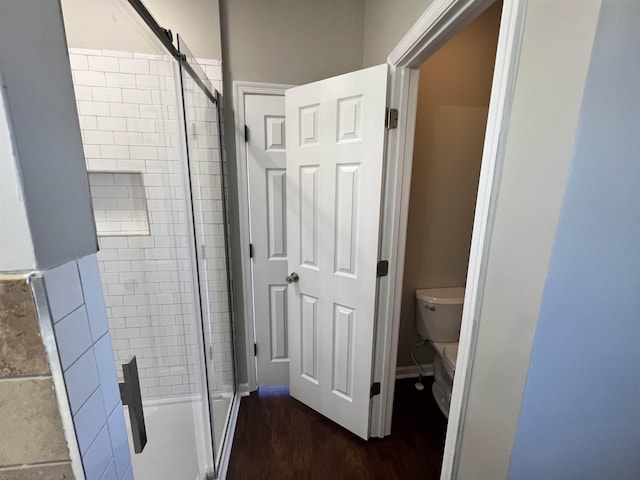 bathroom with hardwood / wood-style floors, a shower with door, and toilet