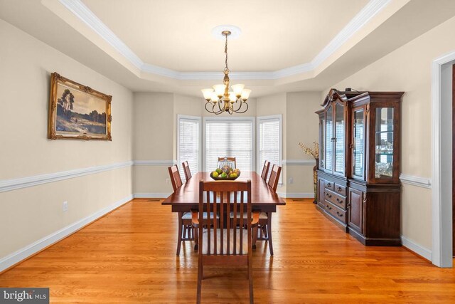 dining space with a chandelier, a tray ceiling, light hardwood / wood-style flooring, and ornamental molding