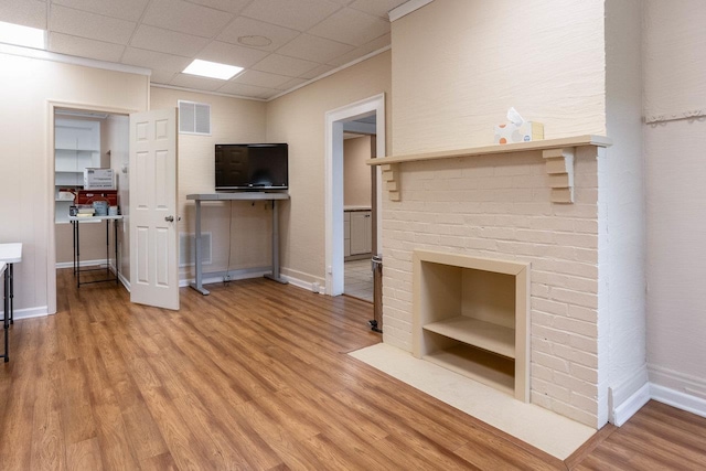 unfurnished living room featuring a drop ceiling, a brick fireplace, and light wood-type flooring