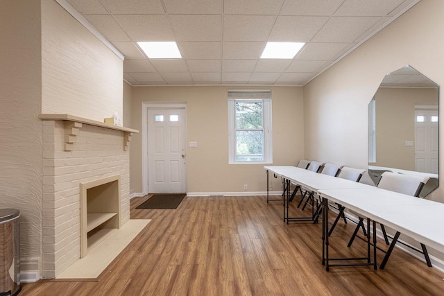 dining area with a brick fireplace, wood-type flooring, and a paneled ceiling