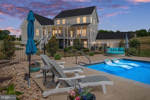 pool at dusk with a sunroom and a patio area