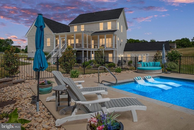 pool at dusk with a sunroom and a patio area