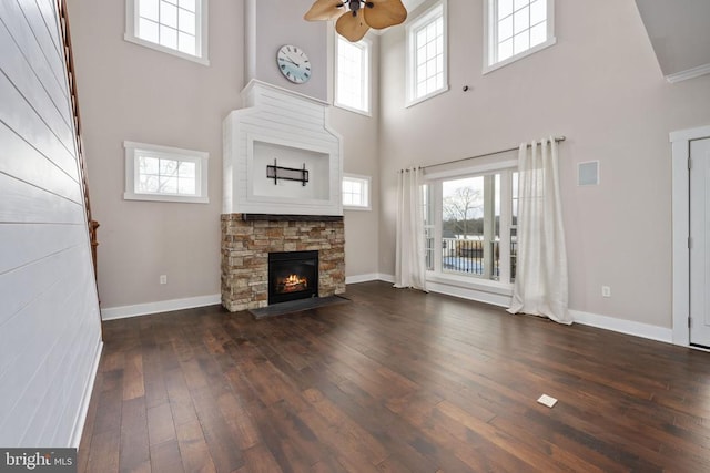 unfurnished living room featuring ceiling fan, a healthy amount of sunlight, dark hardwood / wood-style floors, and a stone fireplace