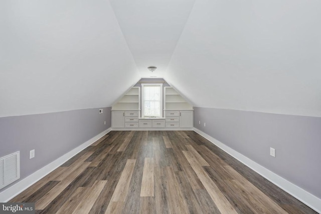 bonus room featuring lofted ceiling, built in shelves, and dark wood-type flooring