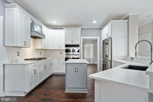 kitchen featuring sink, appliances with stainless steel finishes, custom range hood, white cabinets, and a kitchen island