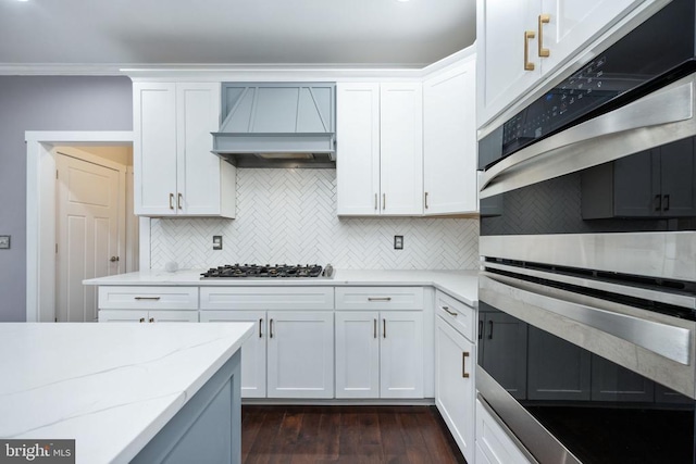 kitchen featuring light stone counters, custom range hood, and white cabinets