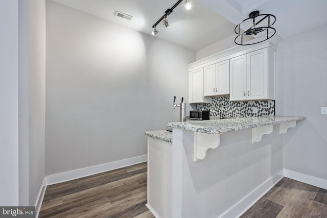 kitchen featuring dark hardwood / wood-style floors, white cabinets, a kitchen breakfast bar, and decorative backsplash