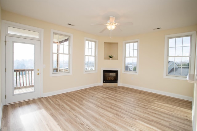 unfurnished living room featuring a ceiling fan, light wood-style floors, baseboards, and a glass covered fireplace