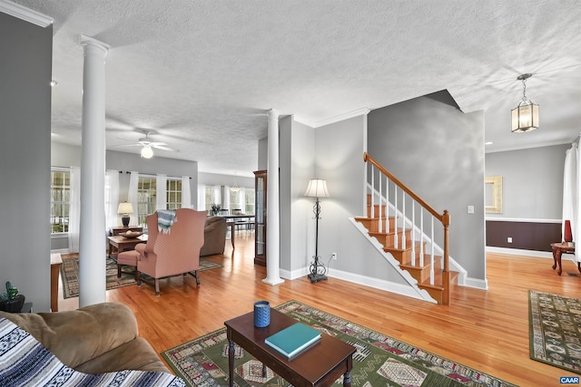 living area featuring wood finished floors, decorative columns, a textured ceiling, stairway, and ceiling fan
