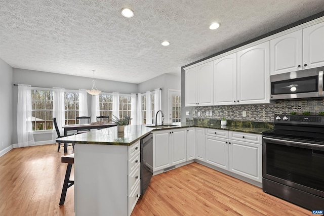 kitchen featuring stainless steel microwave, a peninsula, a sink, light wood finished floors, and range with electric cooktop