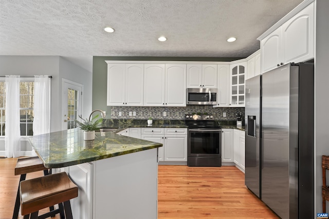 kitchen featuring light wood finished floors, a peninsula, appliances with stainless steel finishes, and a sink