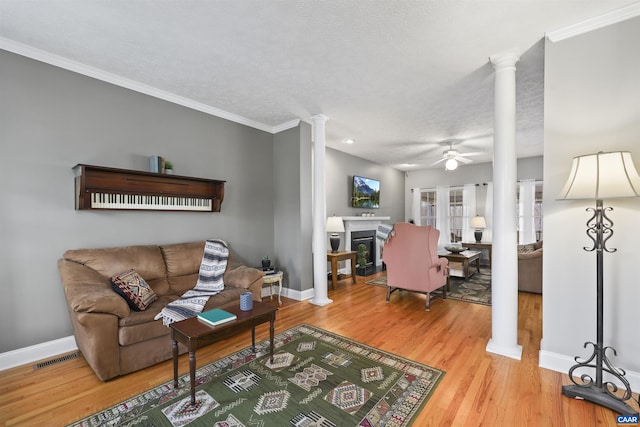 living room with a ceiling fan, baseboards, a glass covered fireplace, and decorative columns