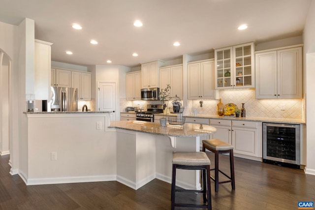 kitchen featuring appliances with stainless steel finishes, wine cooler, light stone counters, decorative backsplash, and glass insert cabinets