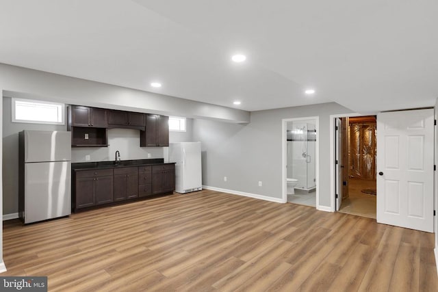 unfurnished living room featuring a sink, light wood finished floors, baseboards, and a healthy amount of sunlight