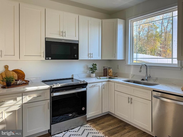 kitchen with stainless steel appliances, a sink, white cabinets, dark wood finished floors, and light stone counters