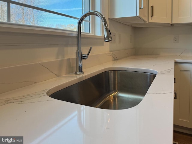 kitchen view of a sink, light stone countertops, and white cabinetry