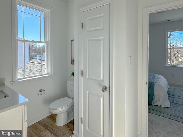 ensuite bathroom featuring toilet, baseboards, vanity, and wood finished floors