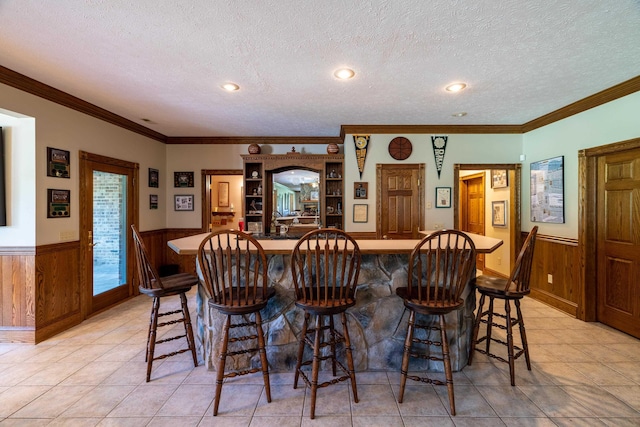 bar featuring crown molding, light tile patterned floors, a textured ceiling, and wood walls