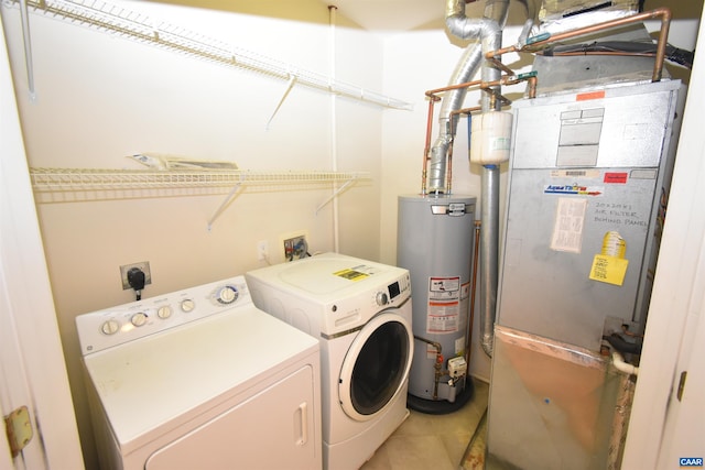 washroom with heating unit, light tile patterned floors, gas water heater, washing machine and clothes dryer, and laundry area