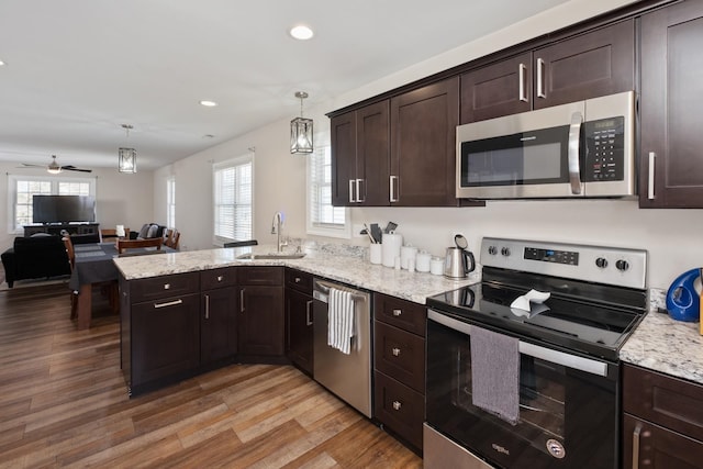 kitchen with light wood finished floors, appliances with stainless steel finishes, a peninsula, dark brown cabinets, and a sink