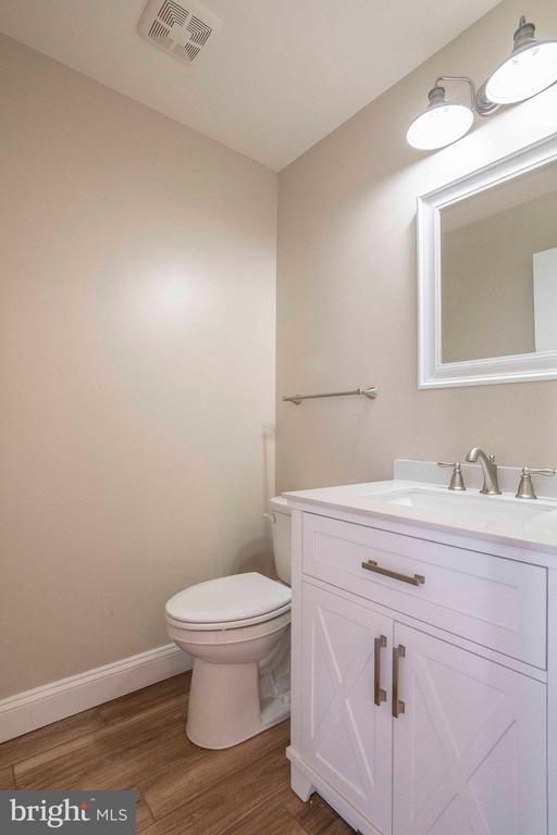 half bath featuring toilet, wood finished floors, vanity, and baseboards