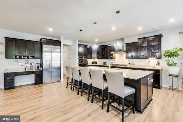 13001 Wipple Ct, Fredericksburg, VA 22407 - kitchen with stainless steel appliances, light wood finished floors, wall chimney range hood, decorative light fixtures, and a breakfast bar