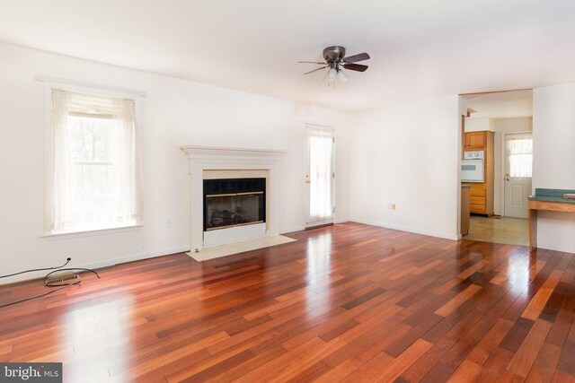 unfurnished living room featuring ceiling fan, baseboards, a fireplace with flush hearth, and wood finished floors