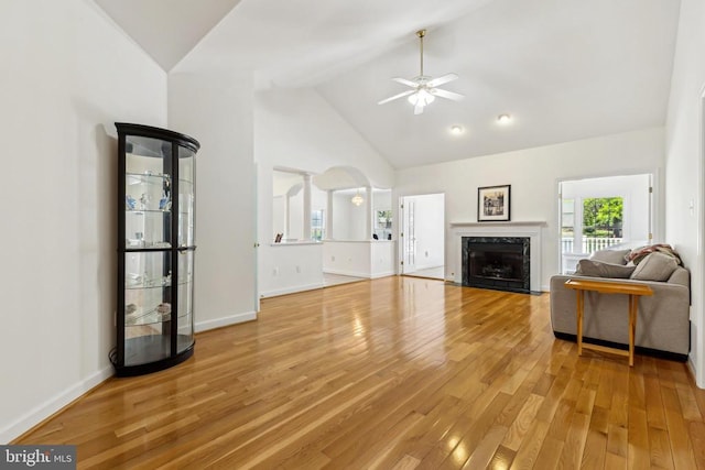 living room featuring light wood-style flooring, a ceiling fan, high vaulted ceiling, baseboards, and a high end fireplace