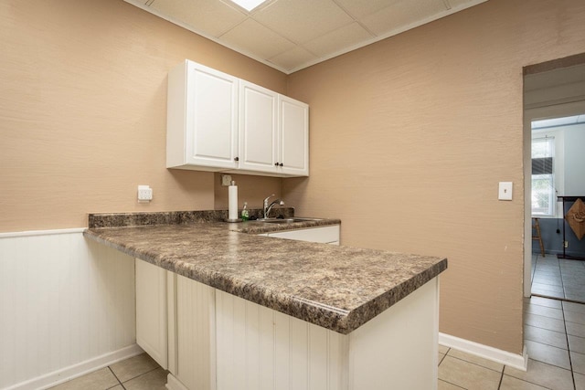 kitchen featuring a peninsula, light tile patterned floors, a sink, dark countertops, and white cabinetry