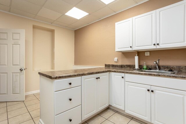 kitchen with a peninsula, dark countertops, light tile patterned floors, and a sink