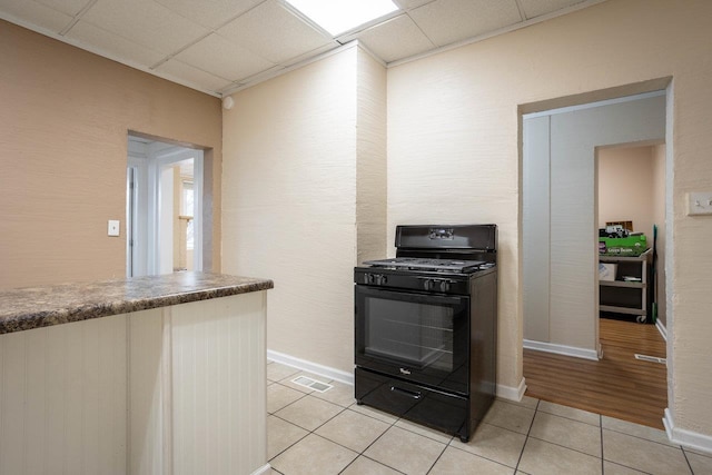 kitchen featuring black gas range oven, a drop ceiling, visible vents, baseboards, and light tile patterned flooring