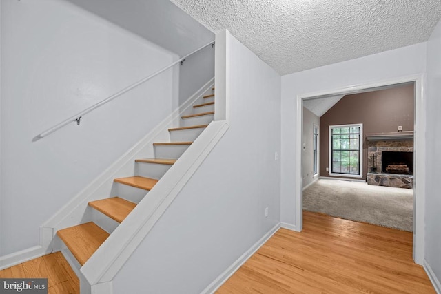 47 Marwood Dr, Palmyra, VA 22963 - stairway featuring wood finished floors, a textured ceiling, a stone fireplace, and vaulted ceiling