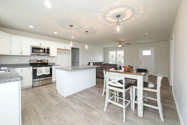 kitchen featuring decorative light fixtures, appliances with stainless steel finishes, a kitchen island, light stone countertops, and white cabinets