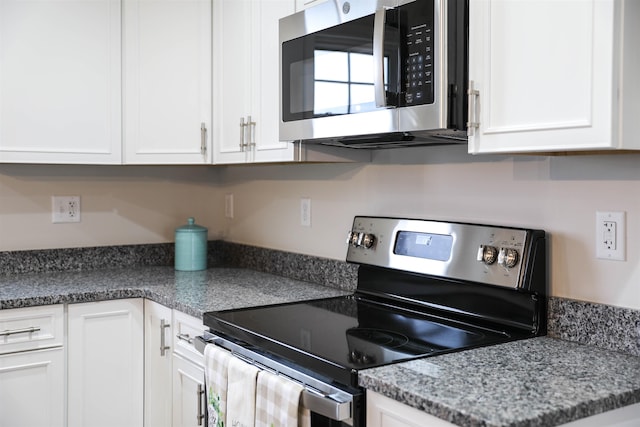 kitchen with stainless steel appliances, white cabinetry, and dark stone counters