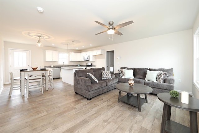 living room featuring ceiling fan, sink, and light wood-type flooring