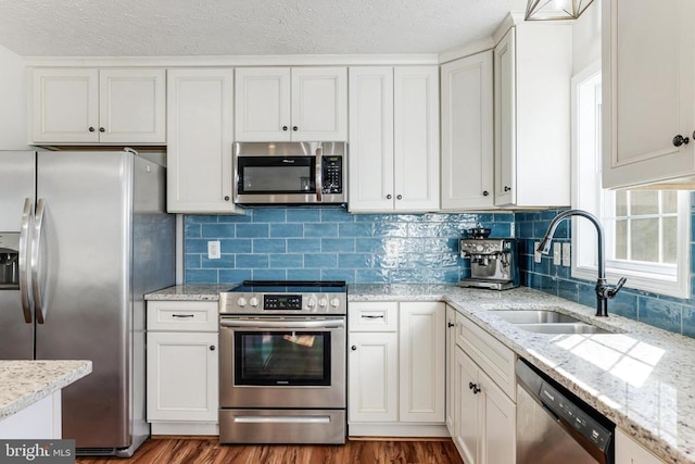  - kitchen with appliances with stainless steel finishes, dark wood finished floors, tasteful backsplash, white cabinetry, and a textured ceiling