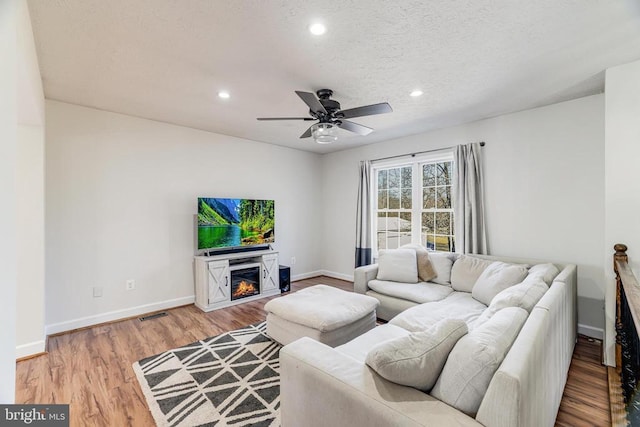  - living room featuring a ceiling fan, a glass covered fireplace, recessed lighting, light wood-type flooring, and a textured ceiling
