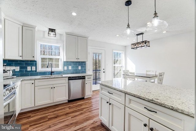  - kitchen featuring stainless steel appliances, wood finished floors, backsplash, a textured ceiling, and pendant lighting