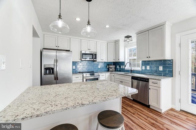  - kitchen with appliances with stainless steel finishes, wood finished floors, a kitchen breakfast bar, backsplash, and light stone counters
