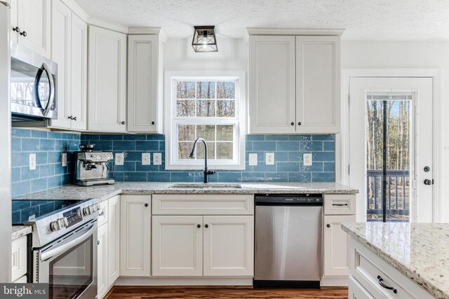  - kitchen featuring stainless steel appliances, a textured ceiling, backsplash, light stone counters, and white cabinetry