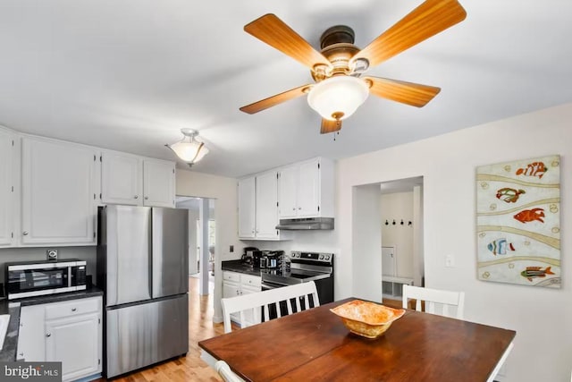 kitchen featuring under cabinet range hood, stainless steel appliances, white cabinetry, light wood-type flooring, and dark countertops