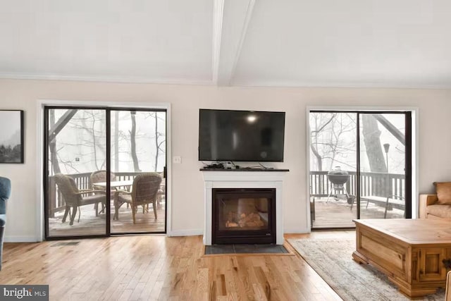 living room with light wood-style flooring, beam ceiling, a fireplace with flush hearth, and a wealth of natural light