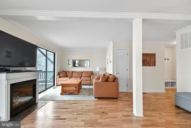 living room featuring light wood-style flooring, baseboards, crown molding, and a glass covered fireplace