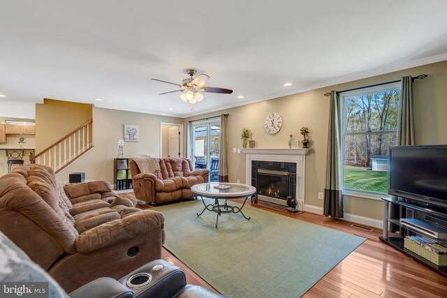  - living area featuring a tile fireplace, wood finished floors, ceiling fan, stairs, and crown molding