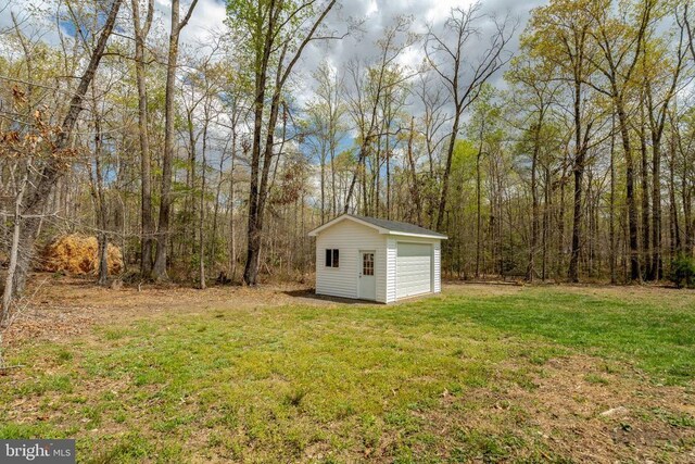  - view of grassy yard with an outbuilding, a detached garage, and a view of trees