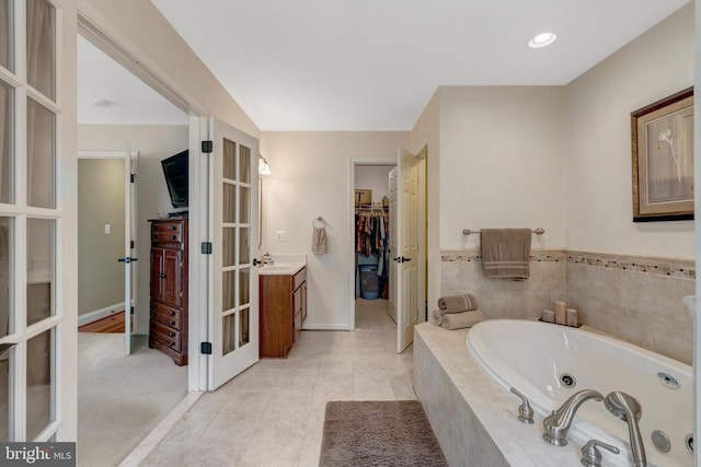  - full bathroom with french doors, a tub with jets, a walk in closet, vanity, and baseboards