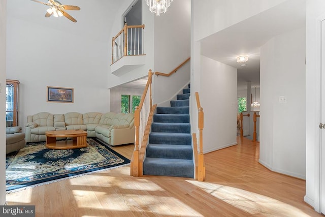  - living area featuring stairway, wood finished floors, a high ceiling, ceiling fan, and a chandelier