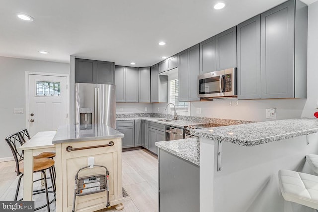  - kitchen featuring stainless steel appliances, gray cabinetry, a kitchen breakfast bar, a peninsula, and light stone counters